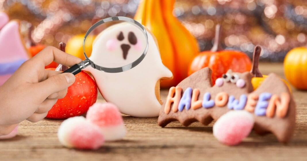 guide-to-finding-sustainable-halloween-candy A hand holds a magnifying glass over a Halloween ghost cookie, illustrating a parent's guide to investigating and finding sustainable Halloween candy.