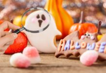Sustainable Halloween Candy: A Parent’s Guide A hand holds a magnifying glass over a Halloween ghost cookie, illustrating a parent's guide to investigating and finding sustainable Halloween candy.